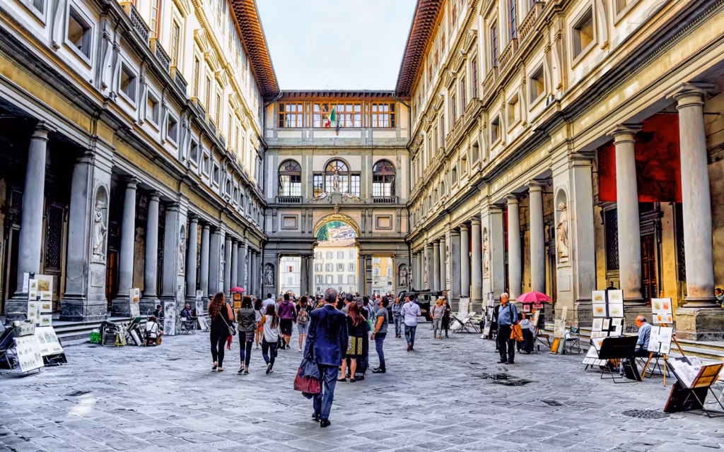 Uffizi Gallery courtyard in Florence, Italy, with people and art stalls. Get your tickets!